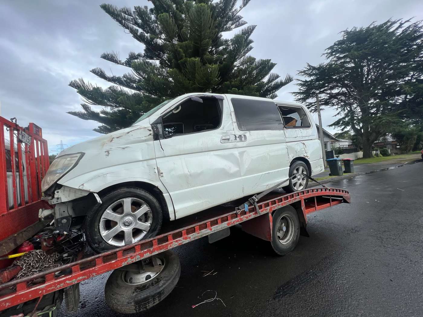 Accident-damaged white van loaded on a red tilt-tray truck for removal in Ashburton