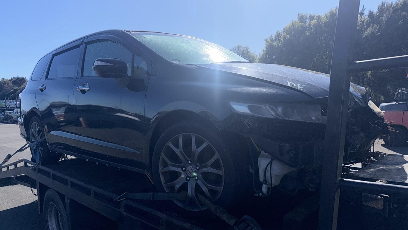Crash-damaged black Honda people-mover with front-end accident damage on a recovery truck