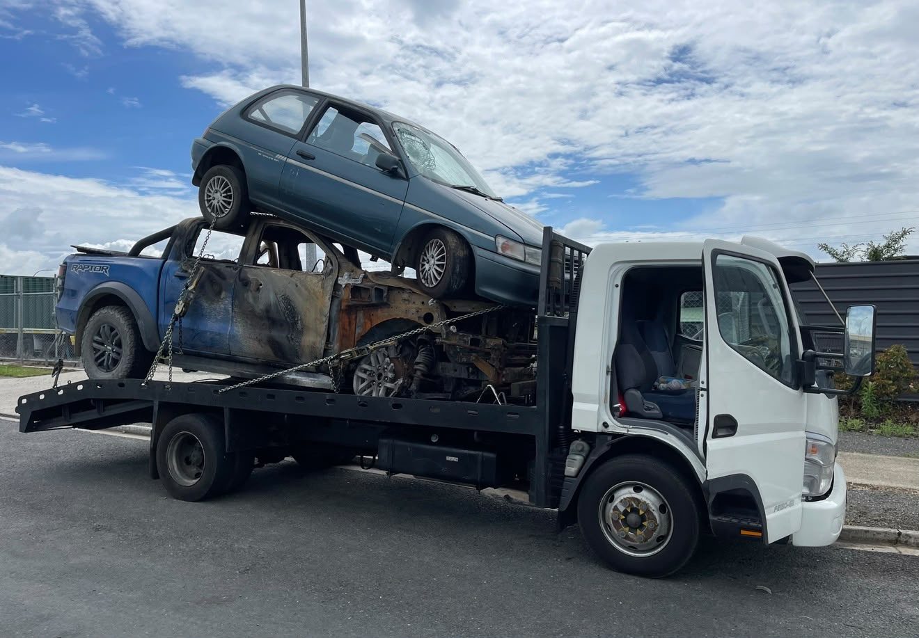 Burnt-out ute and a scrap hatchback loaded on a flatbed truck for cash-for-scrap-cars removal in Ashburton